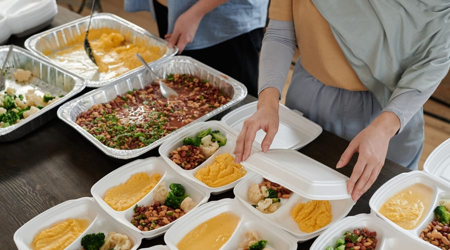 Food service workers portioning beans, cauliflower and broccoli into meal trays for a community meal service